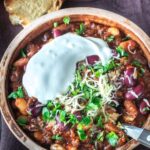 A bowl of hearty turkey chili topped with sour cream, shredded cheese, and fresh herbs, served with a side of crusty bread.