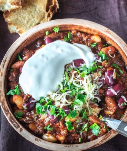 A bowl of hearty turkey chili topped with sour cream, shredded cheese, and fresh herbs, served with a side of crusty bread.