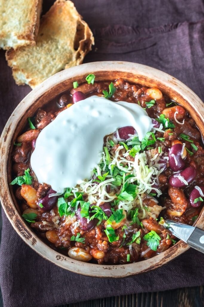 A bowl of hearty turkey chili topped with sour cream, shredded cheese, and fresh herbs, served with a side of crusty bread.